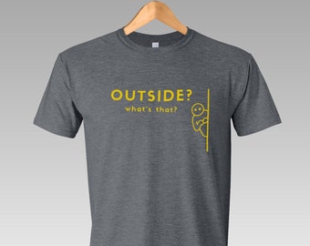 Puede incluir: Una camiseta gris oscuro jaspeada con el texto "OUTSIDE? what's that?" en amarillo. Un pequeño figurín amarillo está mirando por una esquina.