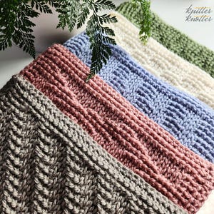 May include: Close-up of five knitted headbands in various colors: gray, dusty rose, light blue, cream, and olive green. Each headband features a unique textured stitch pattern. The headbands are arranged diagonally, with fern leaves in the background.