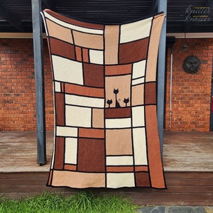 May include: A crocheted throw blanket with a geometric pattern in shades of brown, beige, and cream. The blanket features a silhouette of three cats in the center.