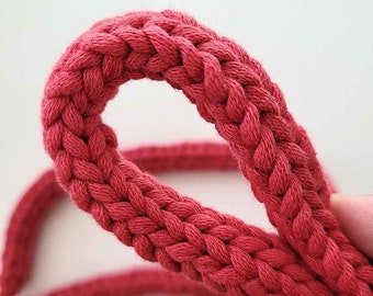 May include: Close-up of a red braided cotton cord. The cord is thick and has a smooth texture. It is perfect for crafting projects.