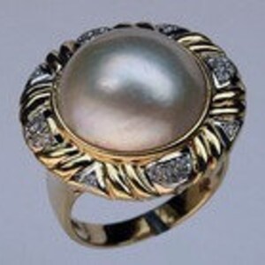 May include: A gold ring with a large white pearl set in a diamond-encrusted bezel. The ring has a twisted band.