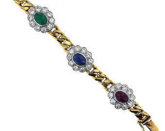 May include: A gold chain bracelet with three oval-shaped gemstones set in diamond-shaped clusters. The gemstones are green, blue, and red.