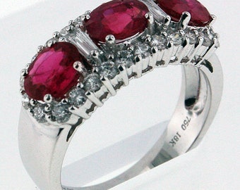 May include: A white gold ring with three oval-shaped ruby gemstones and a band of pave-set diamonds. The ring is marked "18K 750".
