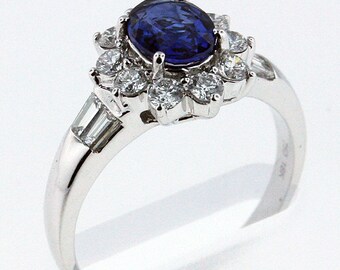 May include: A silver ring with a large blue sapphire surrounded by smaller diamonds. The ring has a delicate band and a floral design.