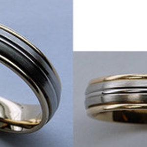 May include: A gold and silver wedding band with a grooved design. The band has three silver grooves on a gold base.