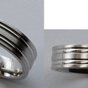 May include: A silver wedding band with three raised lines around the band.