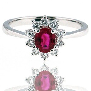 May include: A silver ring with a red oval ruby surrounded by a halo of small diamonds.