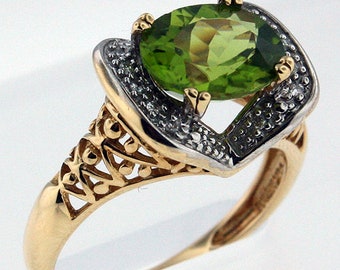 May include: A gold ring with a large green oval gemstone surrounded by smaller white gemstones. The ring has a delicate, intricate design.
