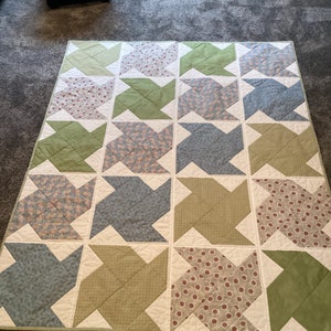 May include: A patchwork quilt with a design featuring green, blue and white fabrics with floral patterns. The quilt is made up of squares and is arranged in a grid pattern.