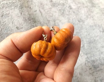 May include: A pair of pumpkin-shaped earrings with silver hooks. The pumpkins are a light orange color and have a slightly textured surface.