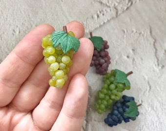 May include: A set of four miniature grape clusters, each with a green leaf. The grapes are green, purple, and blue.