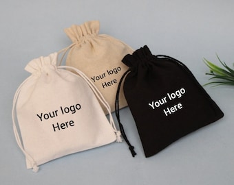Op de afbeelding: Drie trekkoordtassen, een witte, een beige en een zwarte, met de tekst "Your logo Here" erop gedrukt.