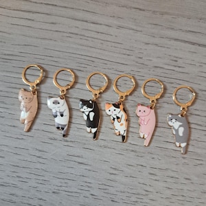 May include: Six cat-shaped keyrings in various colours, including tan, grey, black, and pink. Each keyring features a different cat design. The keyrings have gold-coloured hoops.