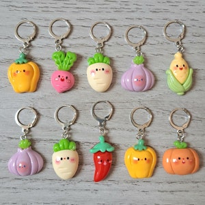 May include: A set of ten metal stitch markers, each featuring a small, colourful resin vegetable charm with a smiling face. The charms include a yellow pepper, pink radish, white turnip, purple garlic, corn, red chilli, and orange pumpkin.