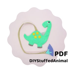 May include: A green felt dinosaur bookmark with yellow spots and a blue felt tail. The bookmark is attached to a brown ribbon. The text "DIYStuffedAnimal" and "PDF" are printed below the bookmark.