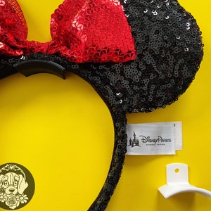 May include: Black and red sequined Minnie Mouse ears headband with a black headband and a red bow. The headband has a white tag that says "Disney Parks Authentic Original".