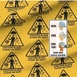 May include: A yellow fabric with a repeating black triangular warning sign pattern featuring a person, a cloud, and the text CAUTION BLACK CLOUD ON SHIFT. An inset shows three light blue scrub caps labeled MENS, EURO, and EURO-PONY with text below.