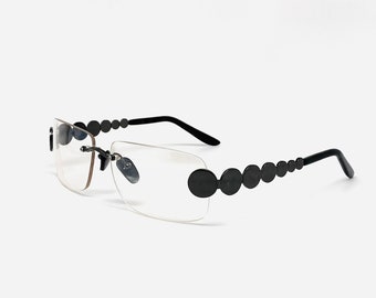 May include: Black rimless glasses with a row of black circles on the side of the frame.