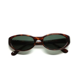 May include: Tortoise shell oval sunglasses with dark green lenses. The sunglasses have the text "HAND POLISHED" printed on the right lens.