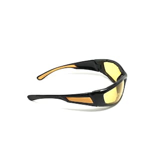 Puede incluir: Gafas de seguridad negras y naranjas con lentes amarillos. Las gafas tienen un diseño envolvente y están hechas de plástico duradero.