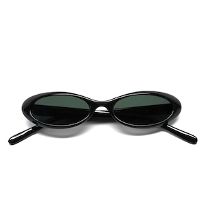 Puede incluir: Gafas de sol ovaladas negras con lentes oscuras. Las gafas tienen un diseño elegante con una montura y patillas finas. Las lentes son de color verde oscuro y la montura es negra brillante.