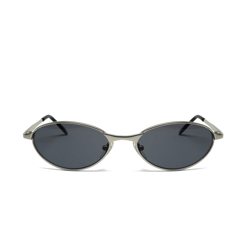 May include: Oval-shaped sunglasses with a silver metal frame and dark lenses. The sunglasses have a sleek, minimalist design, with a thin frame and curved temples. A stylish accessory for eye protection.