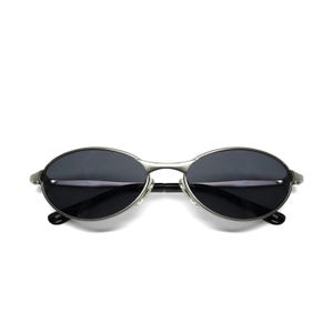 May include: Oval-shaped sunglasses with dark lenses and a silver metal frame. The sunglasses have a sleek, minimalist design, with a thin bridge and temples. The lenses appear to be tinted, providing shade and protection from the sun.