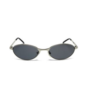 May include: Oval-shaped sunglasses with a silver metal frame and dark gray lenses. The sunglasses have a sleek, minimalist design with thin temples and a classic, retro aesthetic. The lenses are slightly curved.
