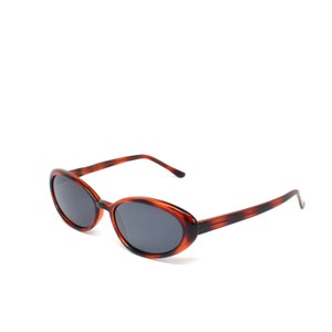 May include: Tortoise shell oval sunglasses with dark lenses.