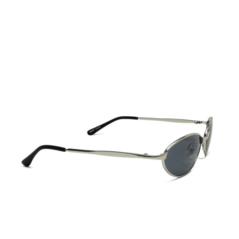 May include: Silver-framed sunglasses with oval lenses and black temples. The sunglasses have a sleek, modern design, suitable for various face shapes. The lenses are a dark gray color, offering protection from the sun.