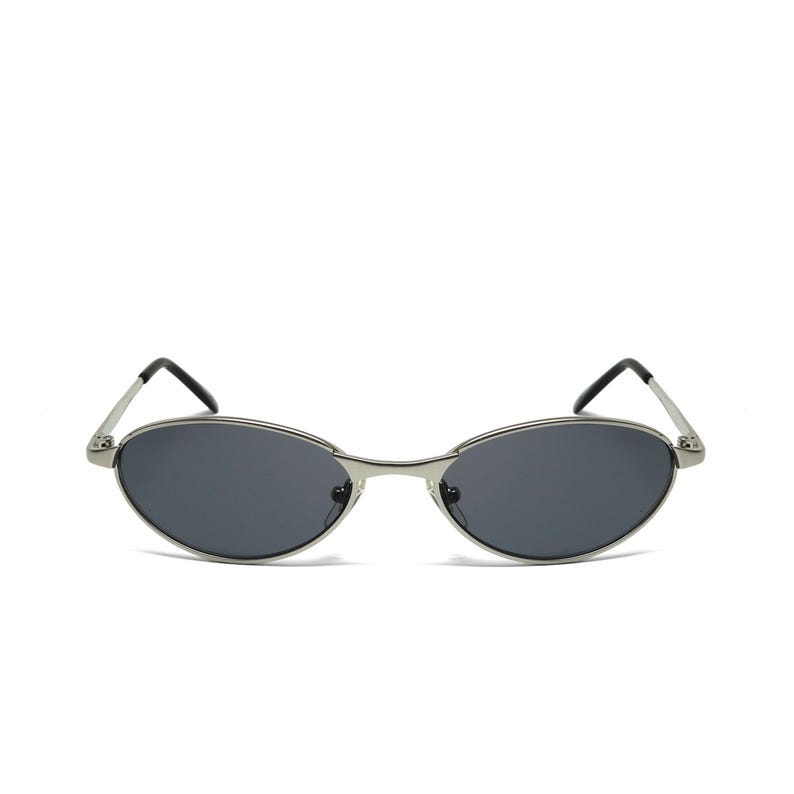May include: Oval-shaped sunglasses with a silver metal frame and dark gray lenses. The sunglasses have a sleek, minimalist design with thin temples and a classic, retro aesthetic. A stylish accessory for eye protection.