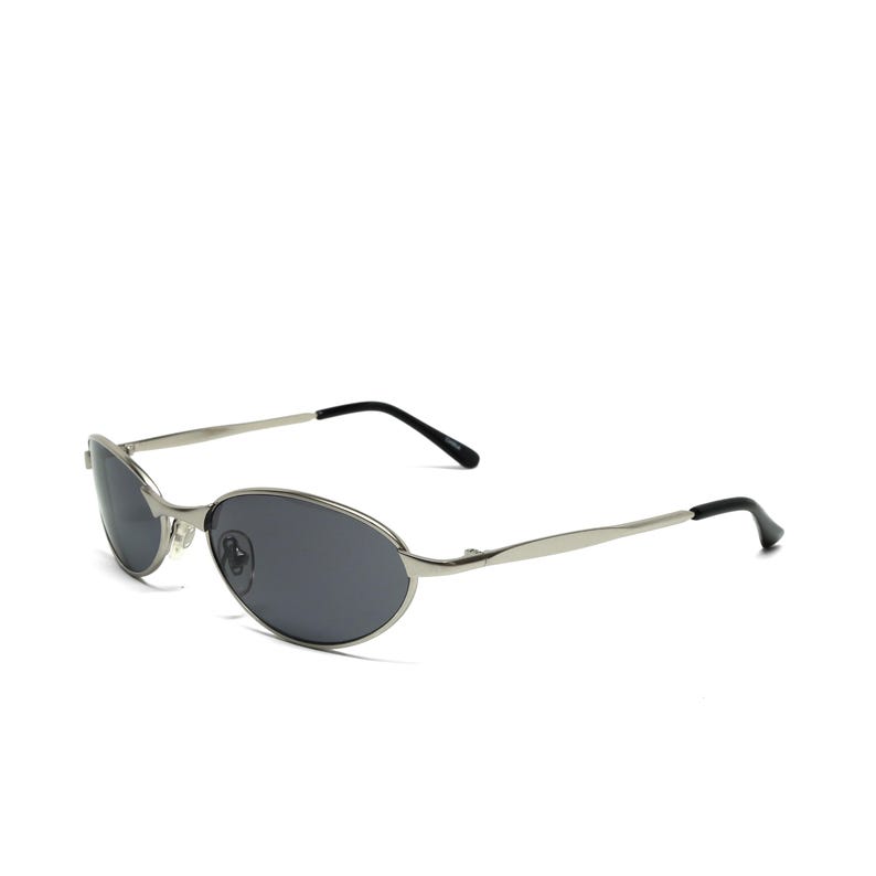 May include: Oval-shaped sunglasses with a silver metal frame and dark gray lenses. The temples are thin and silver, with black tips. The sunglasses are set against a white background.