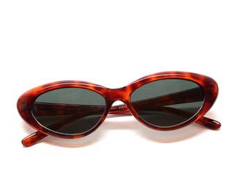 May include: Tortoise shell oval sunglasses with dark lenses. The sunglasses have a subtle brown and gold pattern on the frame.