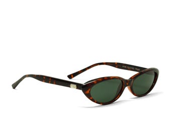 May include: Cat-eye sunglasses featuring a brown and black tortoiseshell pattern frame with dark green lenses. The inner temple arm is clearly marked with the text HAND POLISHED FRAME, and a small metallic accent is visible on the outer hinge.