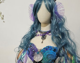 May include: A mannequin wearing a blue and purple crocheted top with seashell accents, a black beaded corset, and a blue wig with a crown of blue crystals. The mannequin is holding a crystal ball in a crocheted glove.