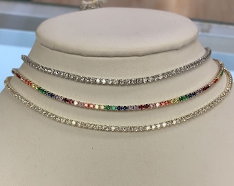 Könnte beinhalten: Drei zarte Halsketten mit einer Reihe kleiner, klarer Steine. Die unterste Halskette hat eine Reihe bunter Steine, die einen Regenbogeneffekt erzeugen.