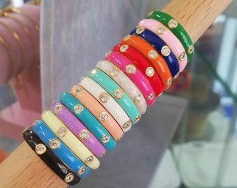 Puede incluir: Pila de anillos de esmalte de colores con pequeños diamantes de imitación transparentes. Cada anillo tiene un color diferente, incluyendo rosa, azul, verde, amarillo, naranja y rojo.