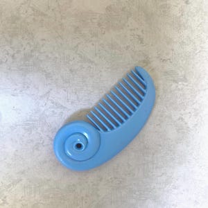 May include: A light blue plastic comb with a spiral design on one end. The comb has evenly spaced teeth and a curved shape. The comb is a solid, single color and appears to be new.