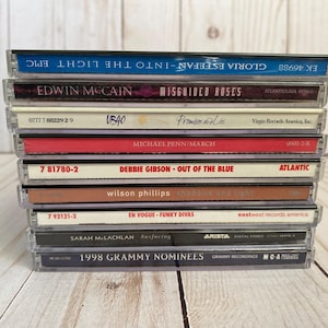 May include: A stack of ten compact discs with various album titles and artist names visible. The CDs are in clear plastic cases, with titles including "Gloria Estefan - Into the Light," "Edwin McCain - Misguided Roses," and "1998 Grammy Nominees."