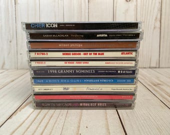May include: A vertical stack of ten music CDs in clear plastic jewel cases. The spines display titles and artists including Cher Icon, Sarah McLachlan Surfacing, Wilson Phillips, Debbie Gibson Out of the Blue, En Vogue Funky Divas, 1998 Grammy Nominees, Gloria Estefan, UB40, Michael Penn, and Edwin McCain.