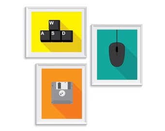 May include: Three framed prints with a retro computer theme. The first print has a yellow background with black keys labeled 'W', 'A', 'S', and 'D'. The second print has a teal background with a black computer mouse. The third print has an orange background with a gray floppy disk.