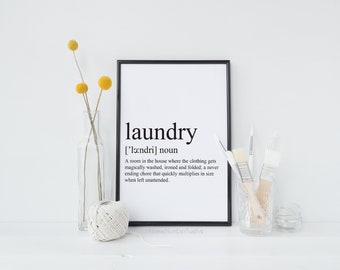 May include: A black framed print with the word "laundry" in bold, followed by its phonetic pronunciation and definition. The definition reads: "A room in the house where the clothing gets magically washed, ironed and folded; a never ending chore that quickly multiplies in size when left unattended."