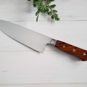 May include: A stainless steel chef's knife with a wooden handle. The handle has a dark brown color and a brass accent.