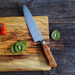 May include: A wooden cutting board with a brown handle knife, a few red tomatoes on a vine, and slices of kiwi fruit.