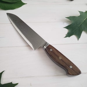 May include: A silver chef's knife with a wooden handle. The knife has a textured blade and a dark brown handle with brass accents.