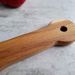 Puede incluir: Un utensilio de cocina de madera con un mango largo y una cabeza redondeada con un agujero en el centro. El utensilio est&aacute; hecho de madera marr&oacute;n claro con un patr&oacute;n de veta natural.