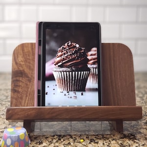 Puede incluir: Un soporte de madera con un acabado marr&oacute;n oscuro sostiene una tableta que muestra una foto de un cupcake de chocolate con chispas. El soporte tiene un borde en la parte delantera y trasera para sujetar la tableta en su lugar.