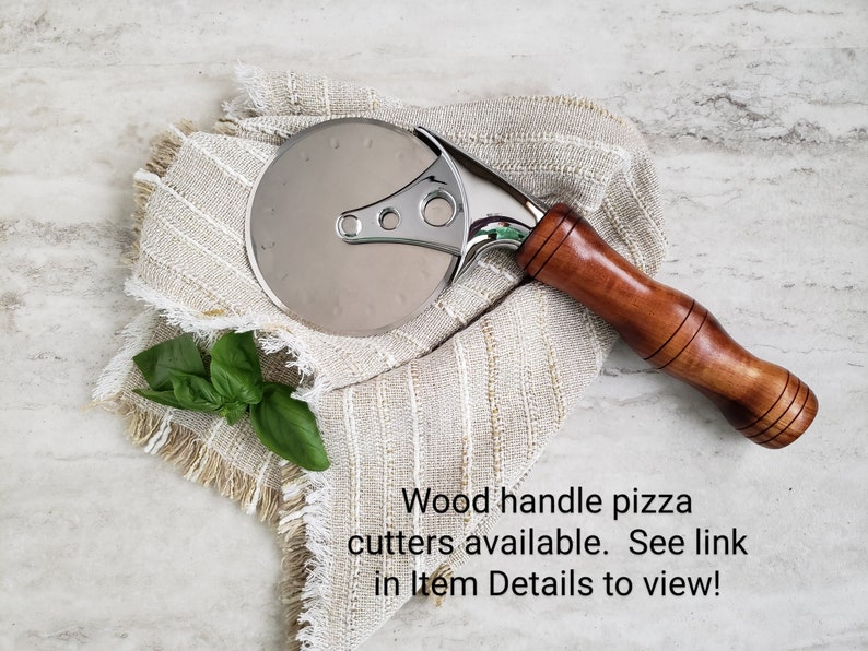 Puede incluir: Un cortador de pizza plateado con mango de madera. El cortador est&aacute; sobre una tela beige con borde de flecos.  Cortadores de pizza con mango de madera disponibles. &iexcl;Ver enlace en Detalles del art&iacute;culo para ver!