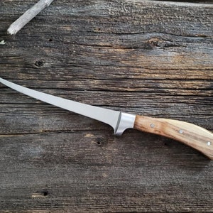 May include: A silver filleting knife with a curved blade and a wooden handle. The handle has a light brown color with darker brown streaks. The knife is lying on a wooden surface.