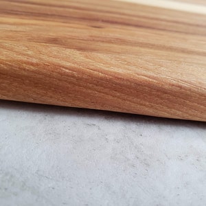Puede incluir: Primer plano de una superficie de madera marr&oacute;n claro con un borde liso ligeramente redondeado. La superficie tiene un patr&oacute;n de veta de madera natural.